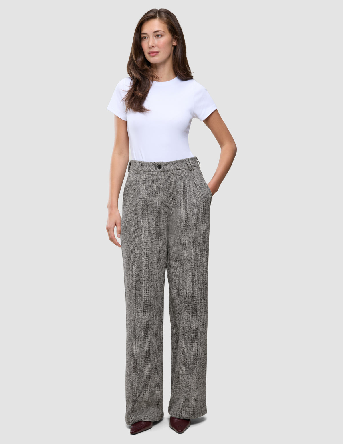 Damenhose Ashryn Wide Domino Herringbone: eine hoch taillierte Hose mit weitem Bein aus grauem Bouclé-Stoff mit Fischgrätenmuster, kombiniert mit einem weißen T-Shirt.