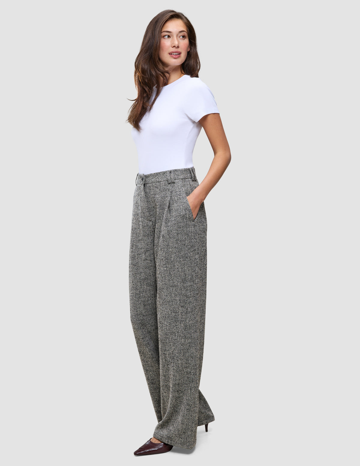 Eine Frau, die ein weißes T-Shirt und die Women Ashryn Pants Wide Domino Herringbone trägt, eine graue, gemusterte Bouclé-Hose mit weitem Bein und Vordertaschen.