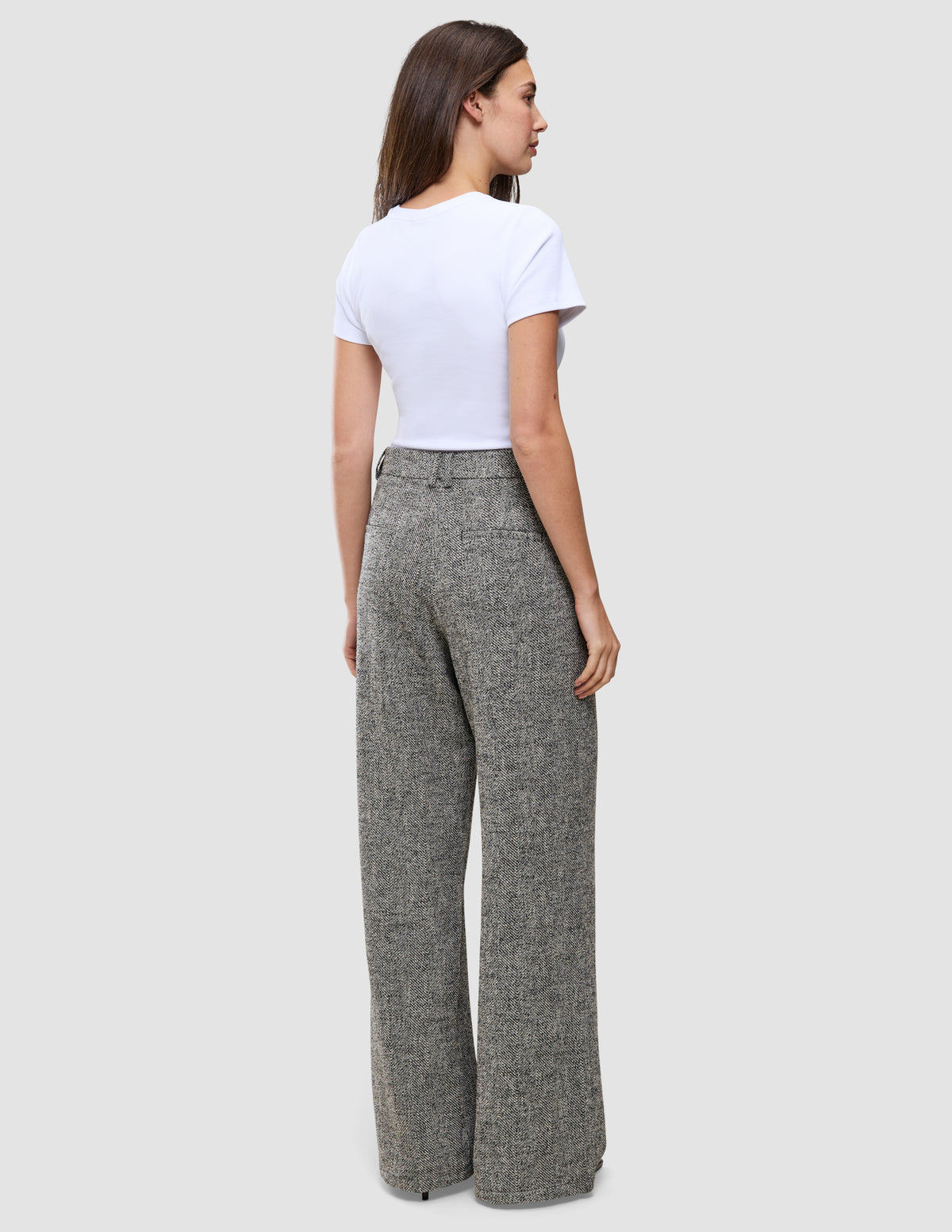 Eine Person, von hinten gesehen, die ein weißes T-Shirt und eine graue, hoch taillierte Hose mit weitem Bein der Marke Women Ashryn Pants Wide Domino Herringbone trägt.