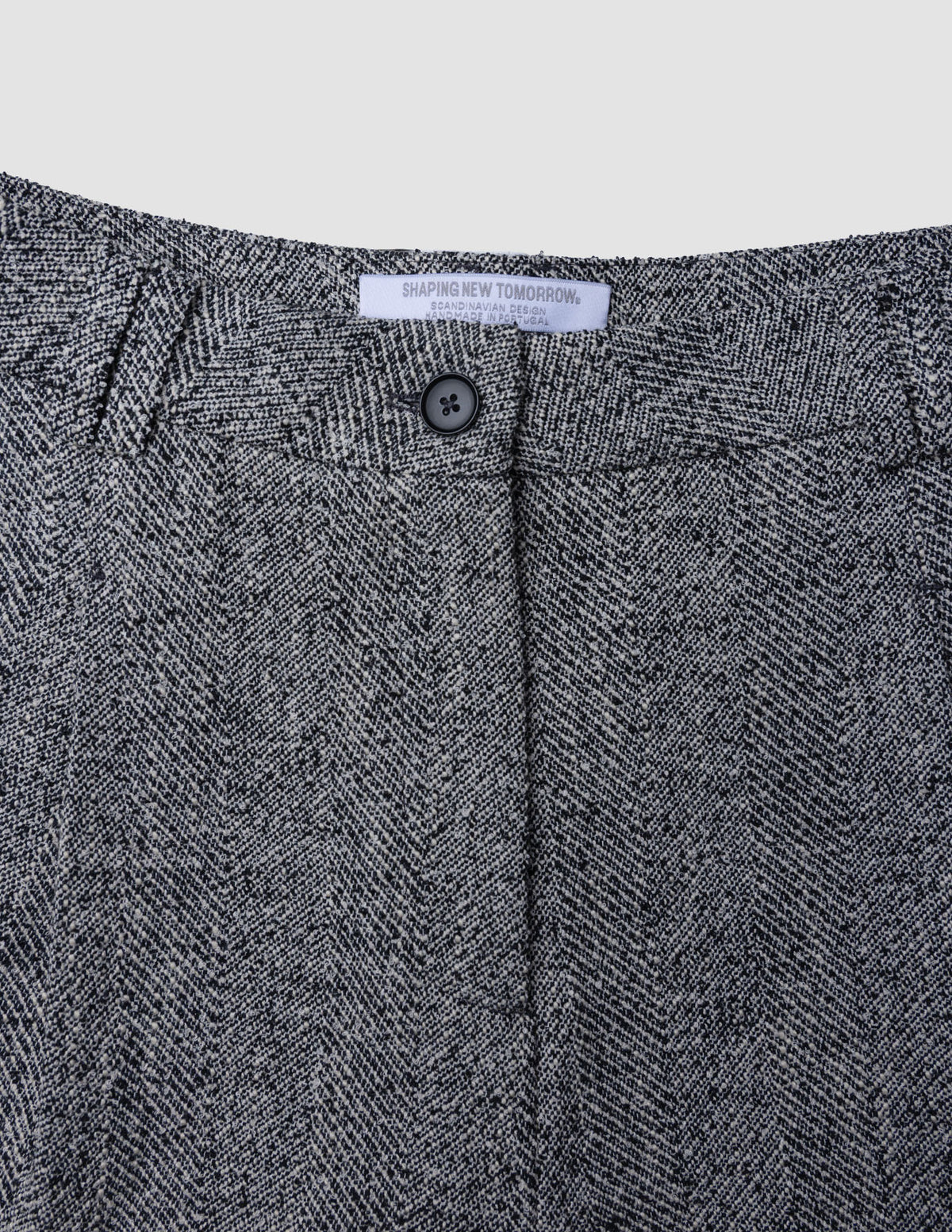 Nahaufnahme des Bunds der Damenhose Ashryn Pants Wide Domino Herringbone aus schwarz-weißem Bouclé mit einem einzelnen Knopf in der Mitte und einem weißen Markenetikett.