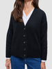 Eine Person, die eine schwarze, grob gestrickte, weiche Wollstrickjacke für Damen über einem weißen Hemd mit Kragen und einer blauen Jeans trägt.