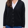 Eine Person, die eine schwarze, grob gestrickte, weiche Wollstrickjacke für Damen über einem weißen Hemd mit Kragen und einer blauen Jeans trägt.