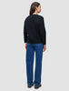 Eine Person, von hinten gesehen, die eine schwarze, dick gestrickte, weiche Damen-Strickjacke aus Wolle, ein weißes Hemd und eine blaue Jeans trägt.