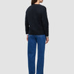 Eine Person, von hinten gesehen, die eine schwarze, dick gestrickte, weiche Damen-Strickjacke aus Wolle, ein weißes Hemd und eine blaue Jeans trägt.