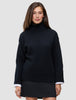 Eine Frau trägt den schwarzen, grob gestrickten, weichen Woll-Rollkragenpullover für Damen aus Merinowolle, an dessen Ärmeln weiße Hemdmanschetten hervorschauen.