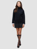 Eine Frau trägt einen schwarzen, grob gestrickten, weichen Wollpullover mit Rollkragen für Damen zusammen mit einem schwarzen Rock, schwarzen, durchsichtigen Kniestrümpfen und schwarzen Pumps.