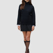 Eine Frau trägt einen schwarzen, grob gestrickten, weichen Wollpullover mit Rollkragen für Damen zusammen mit einem schwarzen Rock, schwarzen, durchsichtigen Kniestrümpfen und schwarzen Pumps.