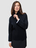 Eine Frau, die einen schwarzen, grob gestrickten, weichen Wollpullover mit Rollkragen für Damen trägt, an dessen Ärmeln weiße Bündchen zu sehen sind.