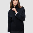 Eine Frau, die einen schwarzen, grob gestrickten, weichen Wollpullover mit Rollkragen für Damen trägt, an dessen Ärmeln weiße Bündchen zu sehen sind.