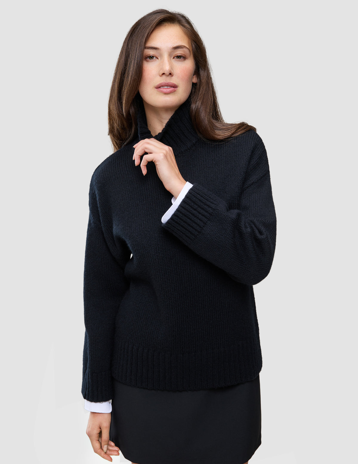 Eine Frau, die einen schwarzen, grob gestrickten, weichen Wollpullover mit Rollkragen für Damen trägt, an dessen Ärmeln weiße Bündchen zu sehen sind.