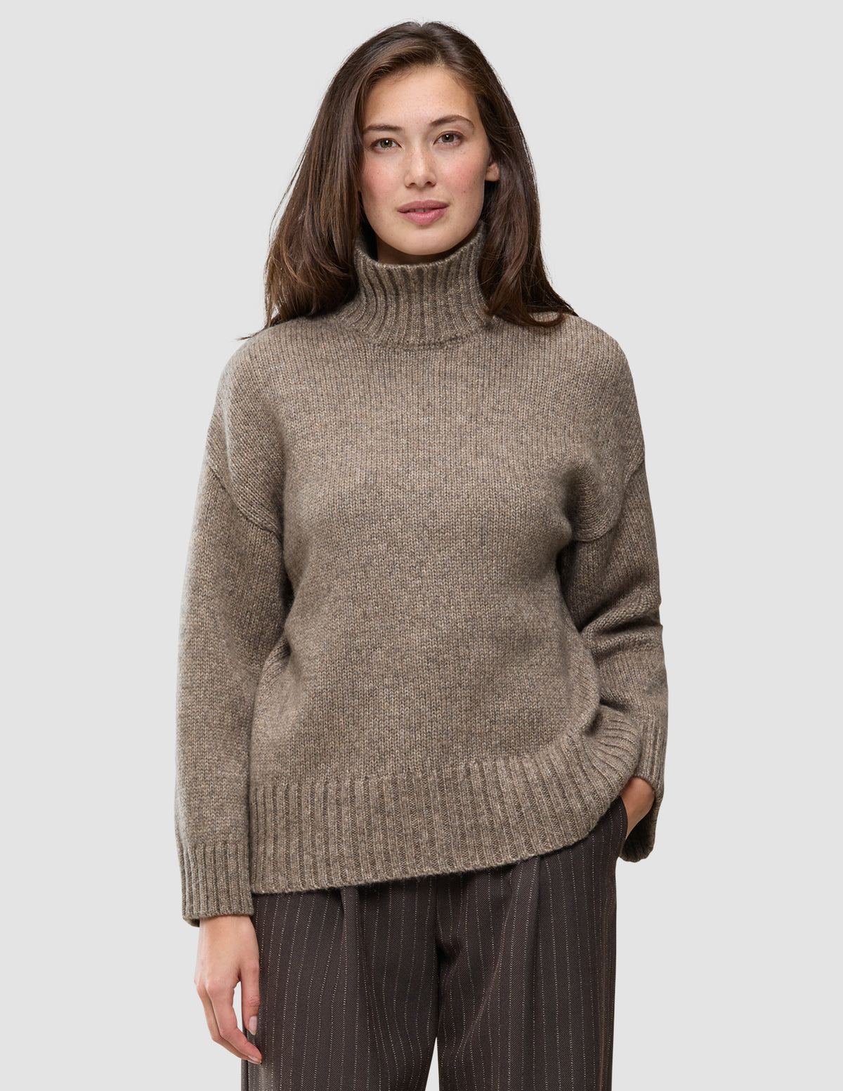 Frau, die einen grob gestrickten, weichen Wollpullover mit Rollkragen in der Farbe Taupe Melange trägt.