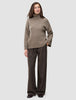 Eine Frau trägt einen dicken, weichen Wollpullover mit Rollkragen in Taupe-Melange und eine braune Nadelstreifenhose.