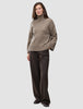 Eine Frau, die einen taupefarbenen, melierten, grob gestrickten, weichen Woll-Rollkragenpullover für Damen und eine weit geschnittene Nadelstreifenhose trägt.