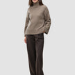 Eine Frau, die einen taupefarbenen, melierten, grob gestrickten, weichen Woll-Rollkragenpullover für Damen und eine weit geschnittene Nadelstreifenhose trägt.