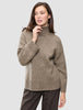 Eine Frau trägt den Women Chunky Soft Wool Knit Turtleneck Taupe Melange, einen taupefarbenen Rollkragenpullover aus Merinowolle mit grobem Strickmuster.