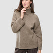 Eine Frau trägt den Women Chunky Soft Wool Knit Turtleneck Taupe Melange, einen taupefarbenen Rollkragenpullover aus Merinowolle mit grobem Strickmuster.