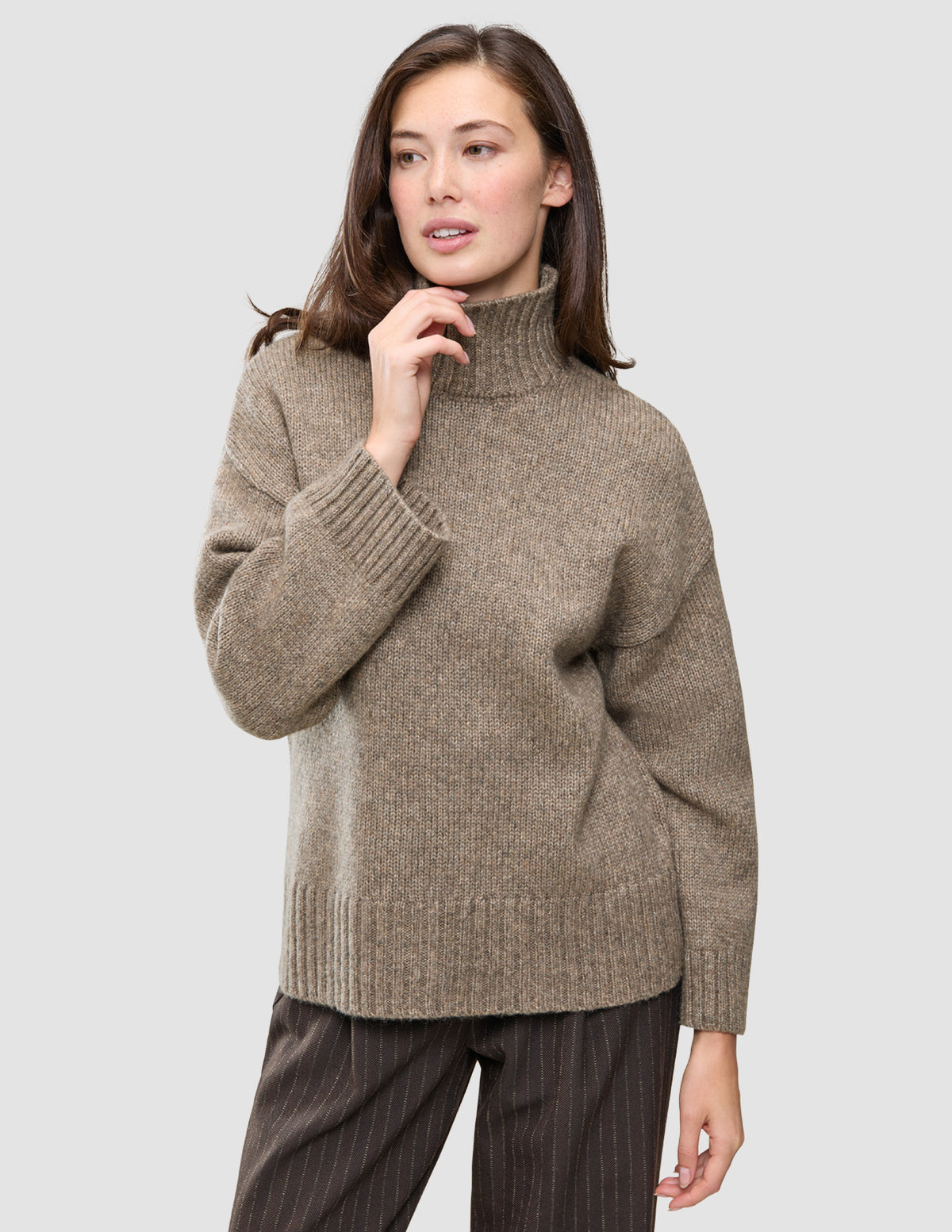 Eine Frau trägt den Women Chunky Soft Wool Knit Turtleneck Taupe Melange, einen taupefarbenen Rollkragenpullover aus Merinowolle mit grobem Strickmuster.