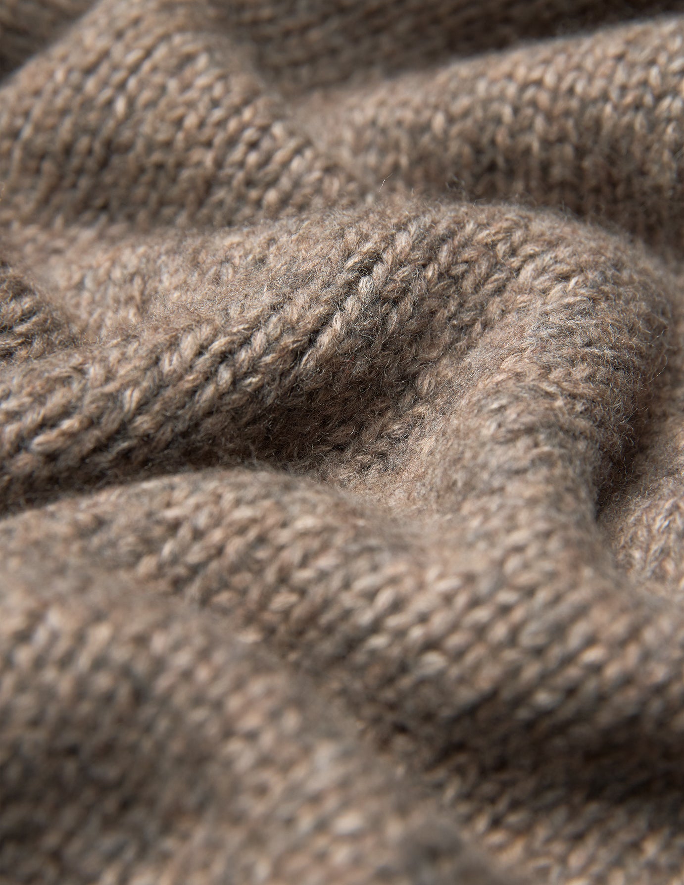 Nahaufnahme des Damen-Rollkragenpullovers aus grobem, weichem Wollstrick in Taupe-Melange, der sich durch einen taupefarbenen, grob gestrickten Stoff mit sichtbarer Rippenstruktur auszeichnet.