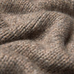 Nahaufnahme des Damen-Rollkragenpullovers aus grobem, weichem Wollstrick in Taupe-Melange, der sich durch einen taupefarbenen, grob gestrickten Stoff mit sichtbarer Rippenstruktur auszeichnet.