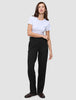 Eine Frau in einem weißen T-Shirt mit Rundhalsausschnitt, einer schwarzen Women GO2-Hose in gerader Passform und dunkelbraunen Loafern, die ein minimalistisches skandinavisches Design widerspiegeln.