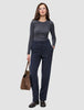 Eine Frau in einem dunkelgrauen Langarmhemd aus Doubleface-Stoff und einer Women GO2 Pants Straight Blue Nights, die eine braune Wildleder-Tragetasche bei sich trägt.
