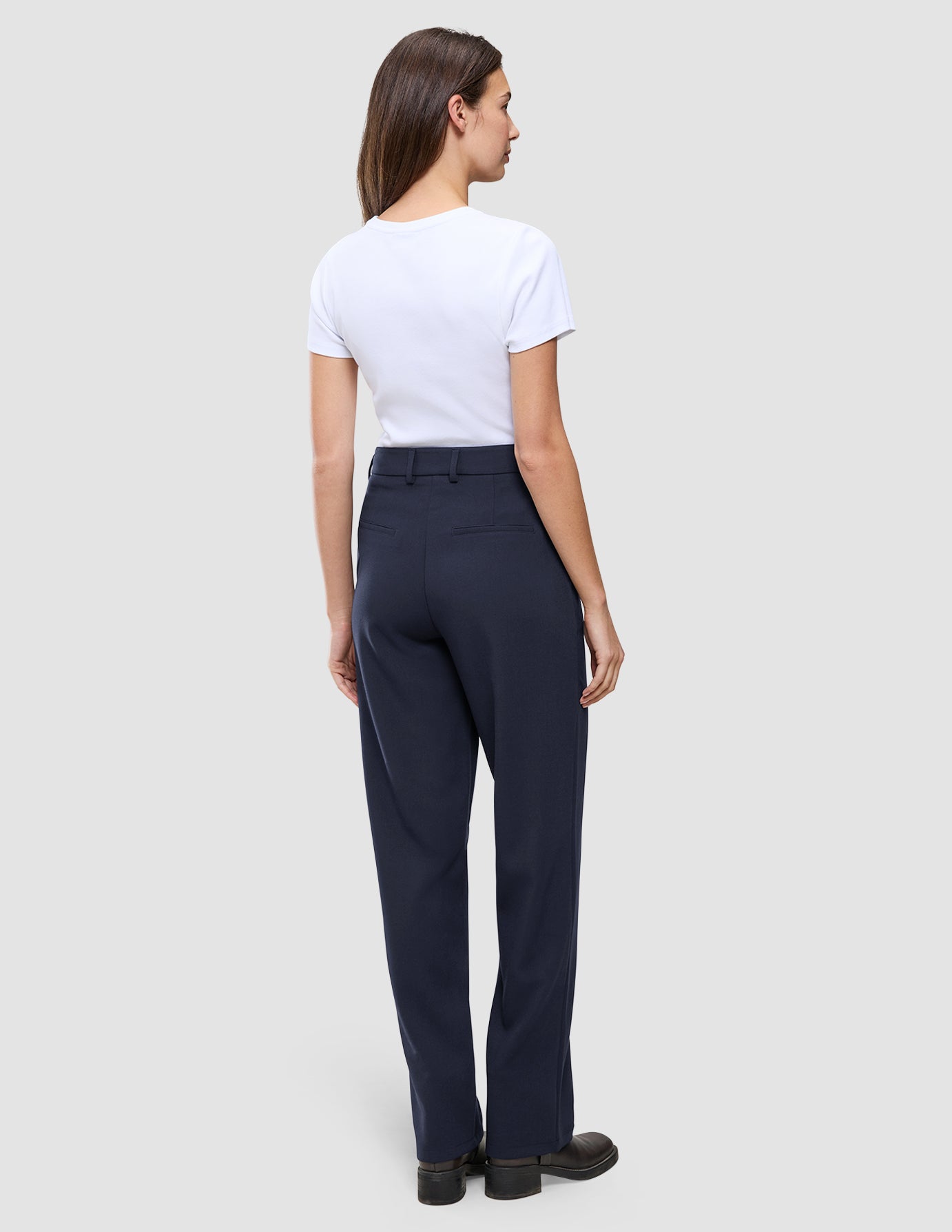Eine Frau, von hinten gesehen, die ein weißes T-Shirt und eine Women GO2 Pants Straight Blue Nights mit geradem Bein, Gesäßtaschen und Gürtelschlaufen trägt.
