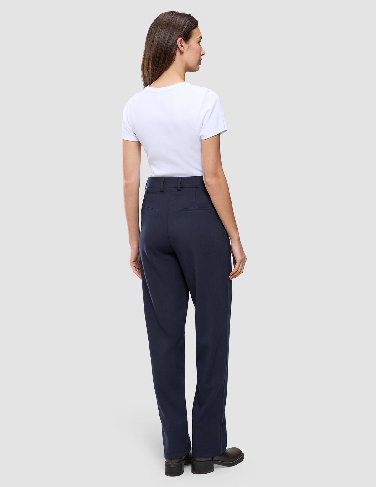 Eine Frau, von hinten gesehen, die ein weißes T-Shirt und eine Women GO2 Pants Straight Blue Nights mit geradem Bein, Gesäßtaschen und Gürtelschlaufen trägt.