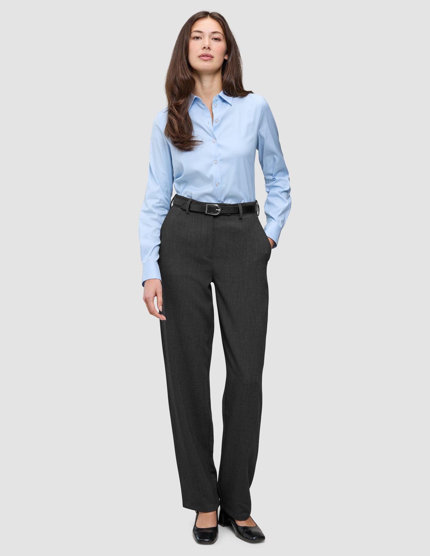 Eine Frau trägt ein hellblaues Hemd, das in eine Women GO2 Pants Straight Dark Grey Melange gesteckt ist, dazu einen schwarzen Gürtel – ein Beispiel für klares skandinavisches Design.