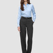 Eine Frau trägt ein hellblaues Hemd, das in eine Women GO2 Pants Straight Dark Grey Melange gesteckt ist, dazu einen schwarzen Gürtel – ein Beispiel für klares skandinavisches Design.