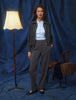 Eine Frau in einer dunkelgrauen Jacke aus Doubleface-Stoff und einem hellblauen Hemd mit Knöpfen, die eine Women GO2 Pants Straight Dark Grey Melange trägt und vor einem blauen Hintergrund steht.
