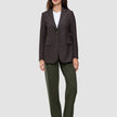 Eine Person trägt einen braunen Blazer mit Nadelstreifen über einem weißen T-Shirt, dazu die Hose Women GO2 Pants Straight Dusty Olive und dunkle Loafer – ein eleganter Look ganz im Sinne des skandinavischen Designs.