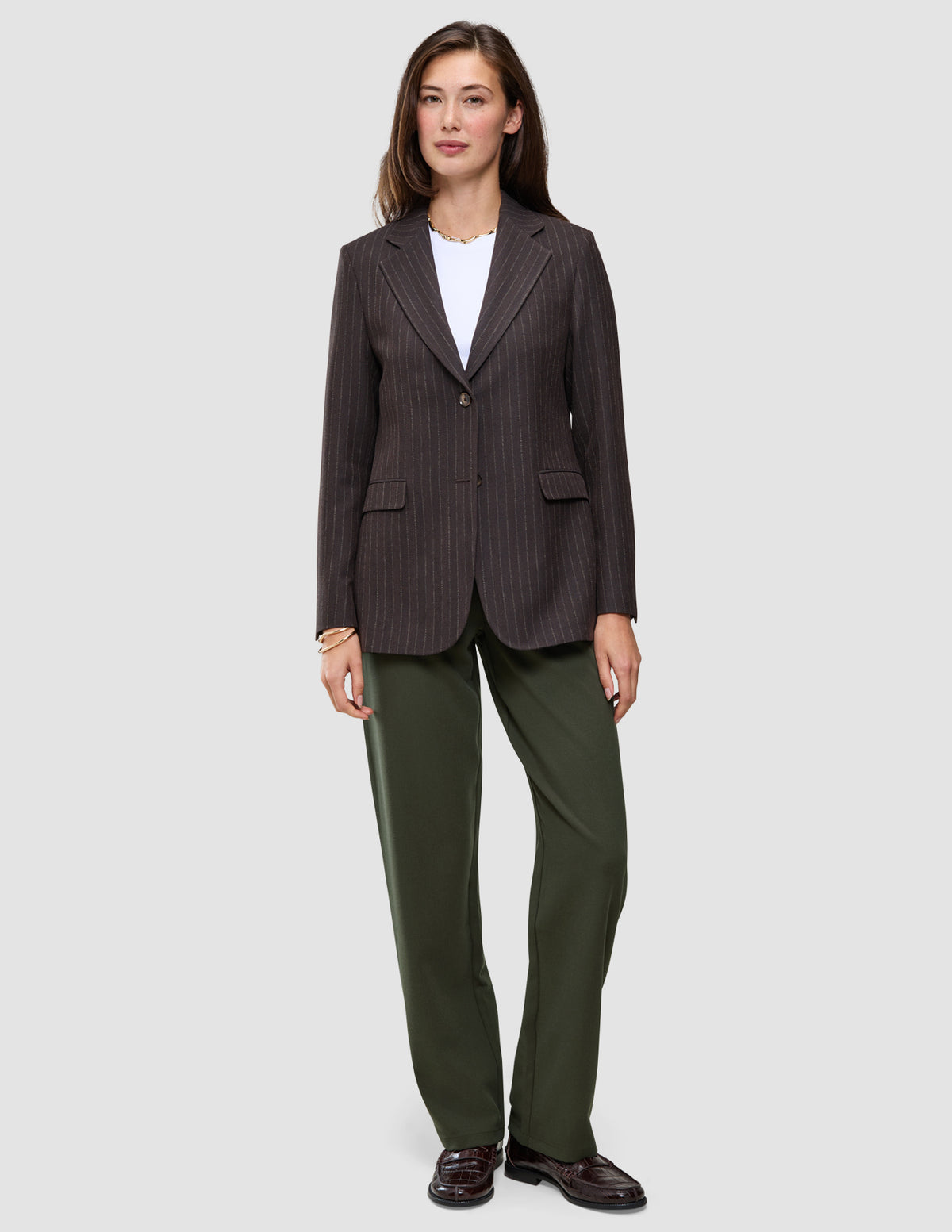 Eine Person trägt einen braunen Blazer mit Nadelstreifen über einem weißen T-Shirt, dazu die Hose Women GO2 Pants Straight Dusty Olive und dunkle Loafer – ein eleganter Look ganz im Sinne des skandinavischen Designs.
