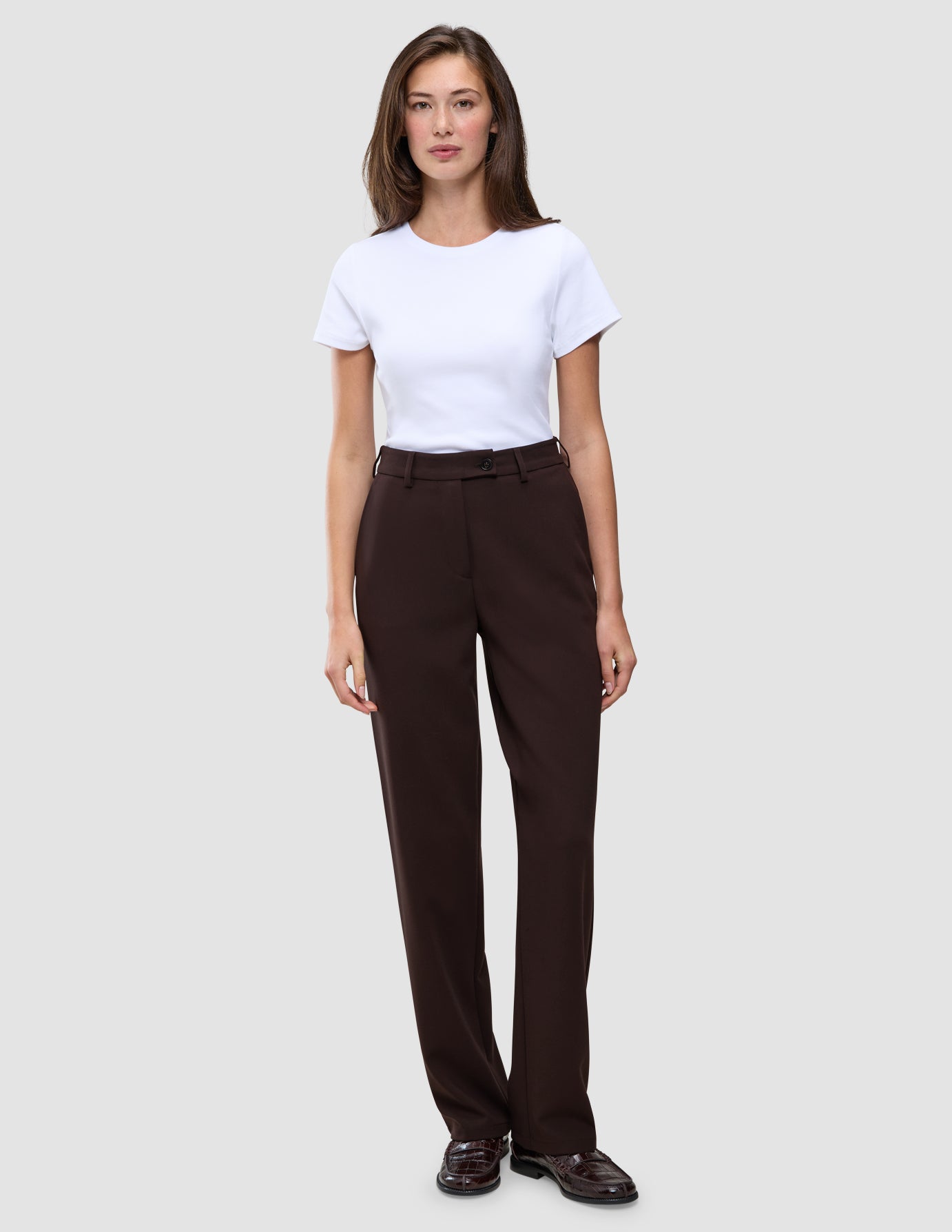 Eine Person, die ein weißes T-Shirt und die Hose Women GO2 Pants Straight Mocha in Dunkelbraun trägt, die sich durch ein schlichtes, skandinavisches Design auszeichnet.