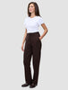 Eine Person, die das minimalistische skandinavische Design verkörpert: Sie trägt ein weißes T-Shirt, die Women GO2 Pants Straight Mocha in Dunkelbraun mit Knopfverschluss und dunkle Loafer.