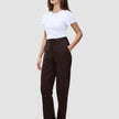 Eine Person, die das minimalistische skandinavische Design verkörpert: Sie trägt ein weißes T-Shirt, die Women GO2 Pants Straight Mocha in Dunkelbraun mit Knopfverschluss und dunkle Loafer.