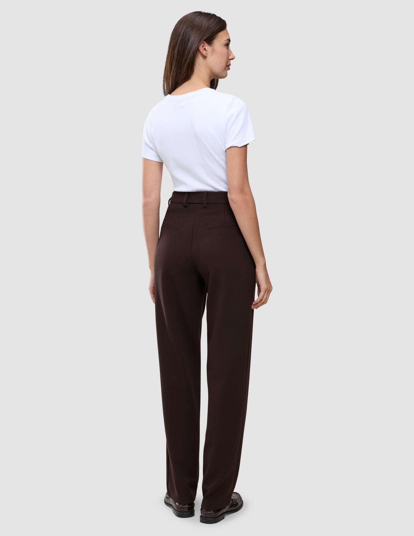Eine Frau, von hinten gesehen, die ein weißes T-Shirt trägt, das in eine dunkelbraune Women GO2 Pants Straight Mocha mit hoher Taille und geradem Beinschnitt gesteckt ist.
