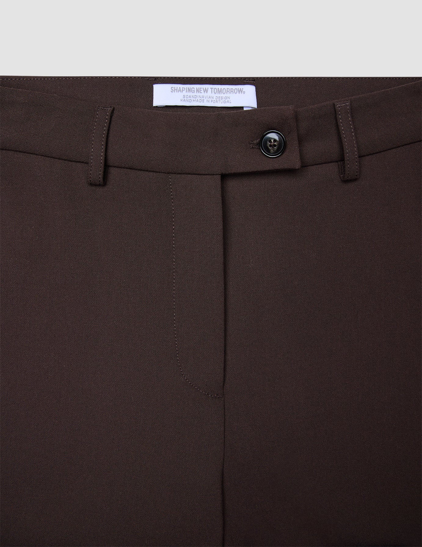 Nahaufnahme der Women GO2 Pants Straight Mocha aus Doubleface-Material, mit Knopfverschluss, Gürtelschlaufen und einem weißen Markenetikett auf der Innenseite.