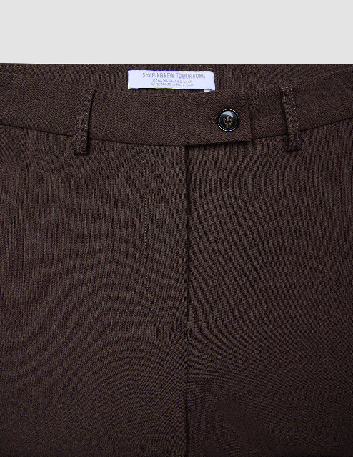 Nahaufnahme der Women GO2 Pants Straight Mocha aus Doubleface-Material, mit Knopfverschluss, Gürtelschlaufen und einem weißen Markenetikett auf der Innenseite.