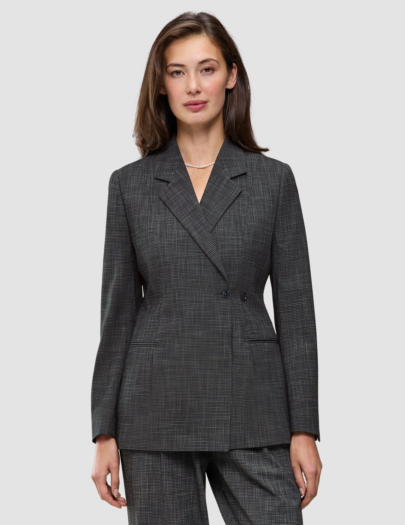 Eine Frau trägt den Women Nara Blazer Fitted Black Check, einen taillierten, schwarz-weiß karierten Zweireiher-Blazer mit 360°-Stretch.