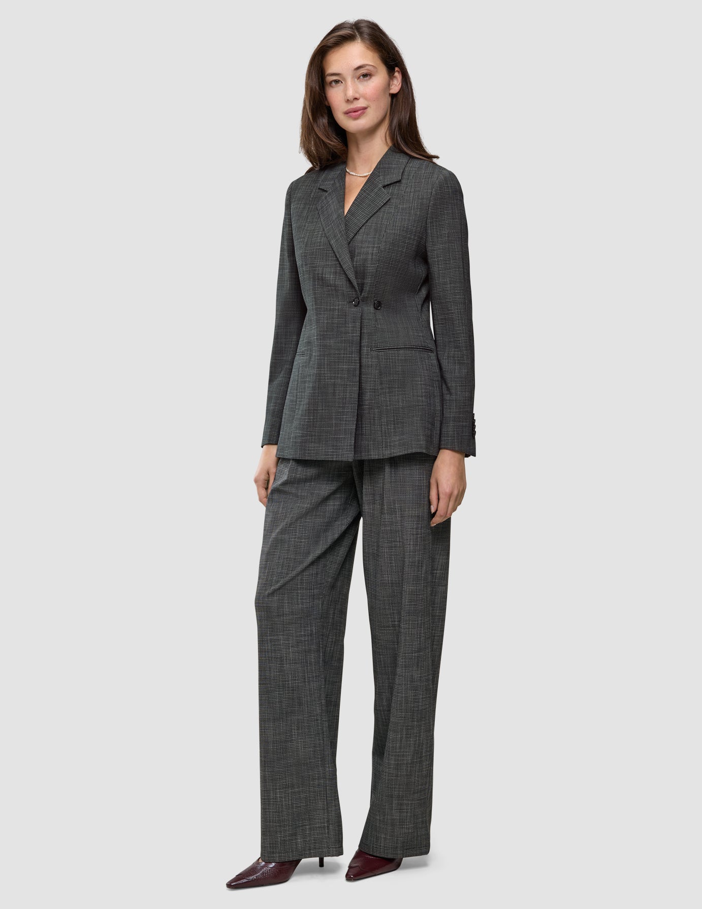 Eine Frau trägt einen Women Nara Blazer Fitted Black Check in Anthrazitgrau sowie eine dazu passende Hose mit weitem Bein und dezentem Karomuster, die ein elegantes, skandinavisch inspiriertes Design präsentieren.