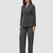 Eine Frau trägt einen Women Nara Blazer Fitted Black Check in Anthrazitgrau sowie eine dazu passende Hose mit weitem Bein und dezentem Karomuster, die ein elegantes, skandinavisch inspiriertes Design präsentieren.