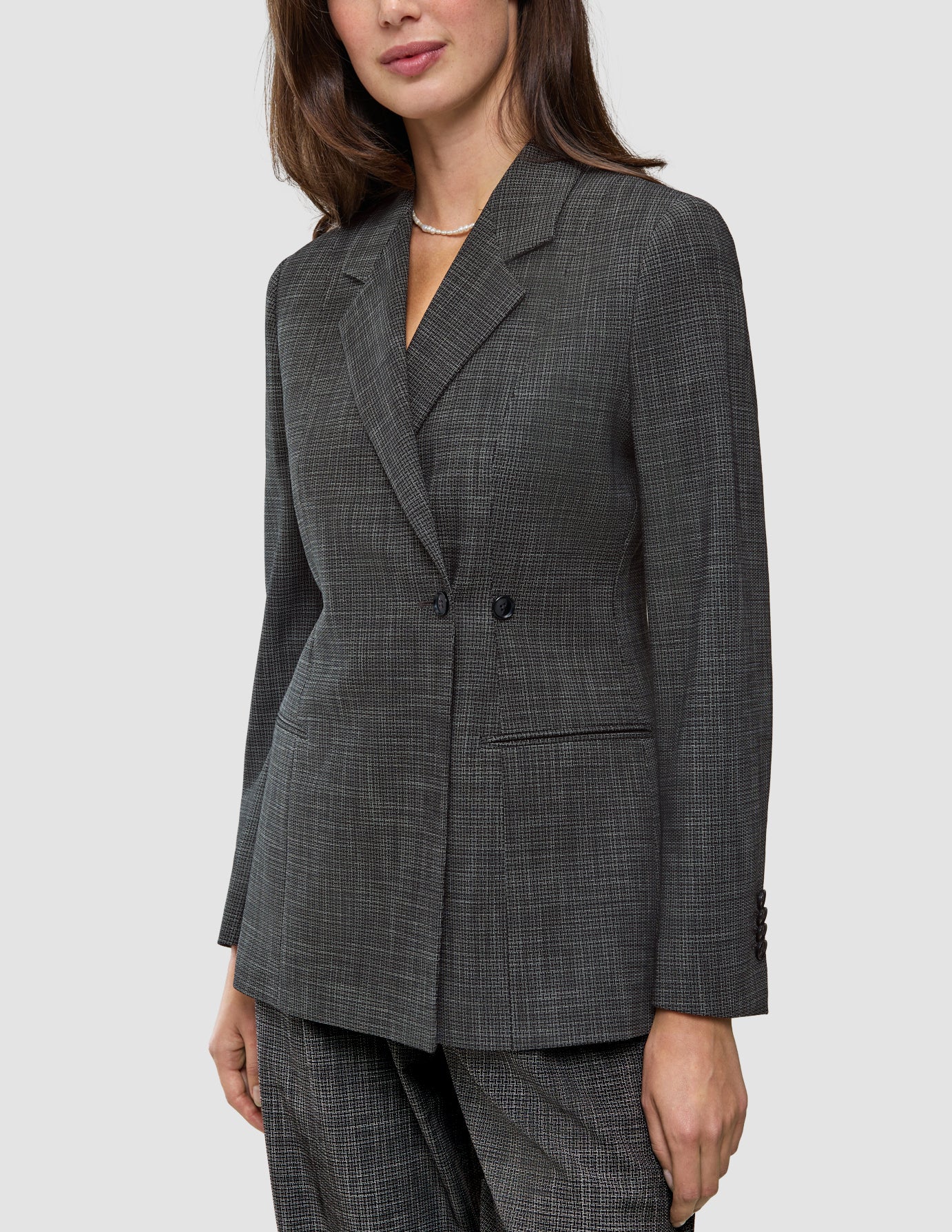 Eine Person, die einen Women Nara Blazer Fitted Black Check trägt, einen taillierten Zweireiher-Blazer mit dunkelgrauem Mikrokaromuster und 360°-Stretch.