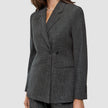 Eine Person, die einen Women Nara Blazer Fitted Black Check trägt, einen taillierten Zweireiher-Blazer mit dunkelgrauem Mikrokaromuster und 360°-Stretch.