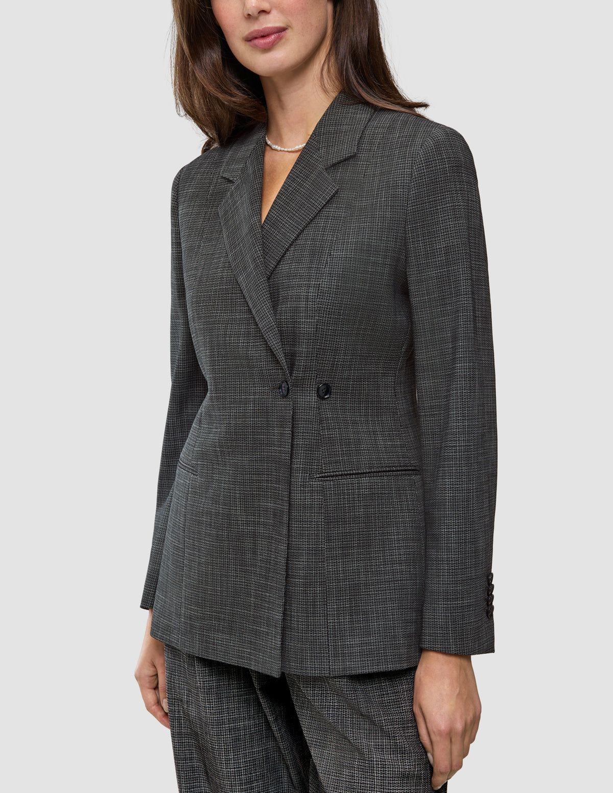 Eine Person, die einen Women Nara Blazer Fitted Black Check trägt, einen taillierten Zweireiher-Blazer mit dunkelgrauem Mikrokaromuster und 360°-Stretch.