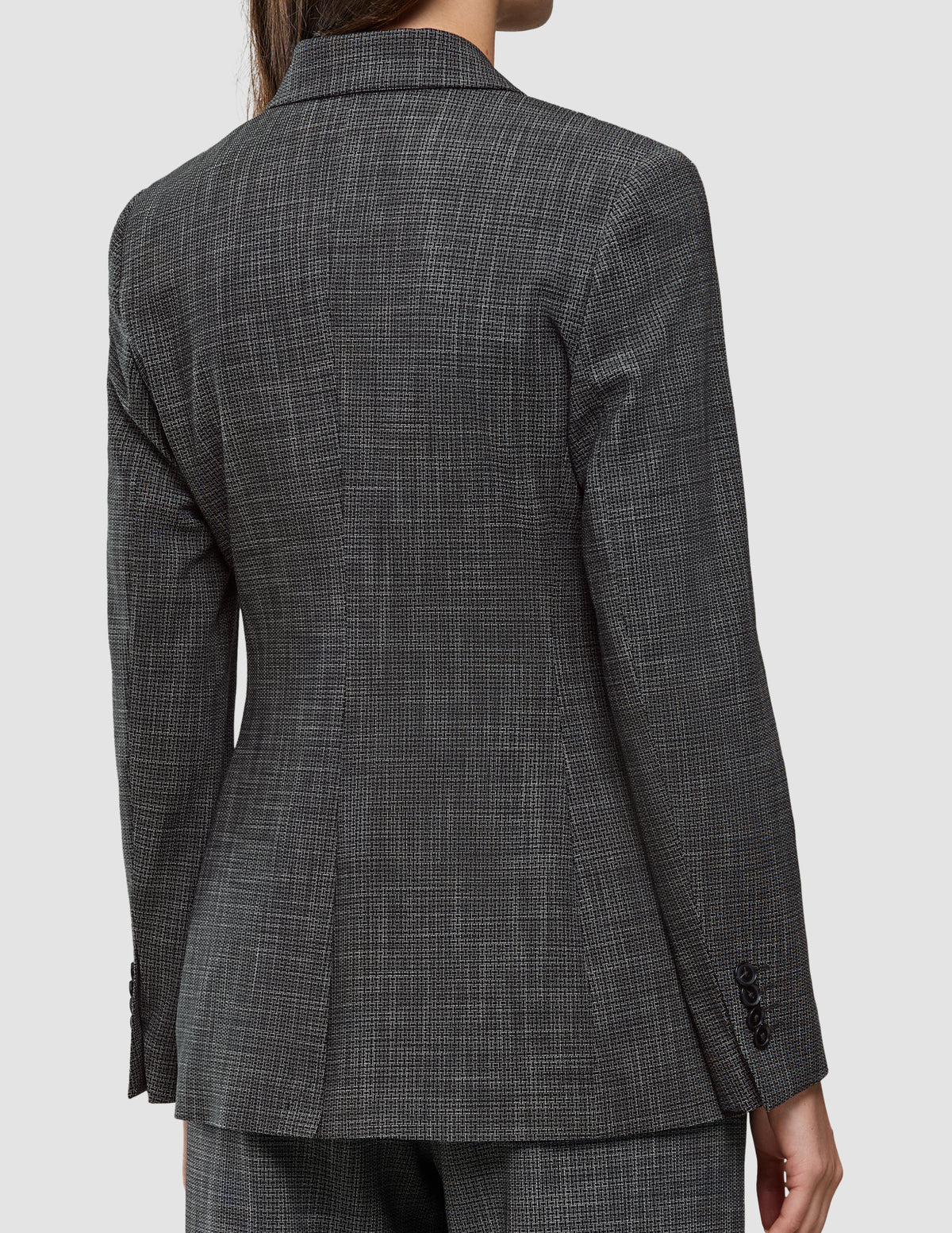 Eine Person, von hinten gesehen, die einen Women Nara Blazer Fitted Black Check trägt – ein taillierter Blazer mit schwarz-weißem Mikrokaromuster und 360°-Stretch.