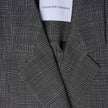 Nahaufnahme eines Women Nara Blazer Fitted Black Check mit einem maßgeschneiderten schwarz-weißen Karomuster und einem weißen Etikett im Nackenbereich, auf dem SHAPING NEW TOMORROW steht.