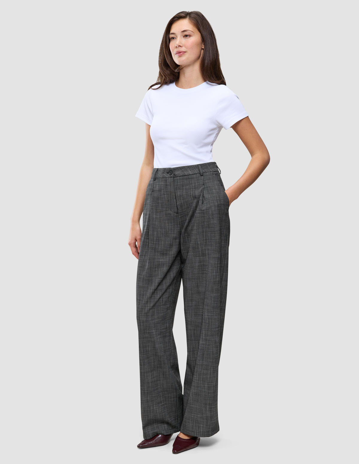 Eine Frau, die ein schlichtes weißes T-Shirt und die Women Nara Pants Wide Black Check trägt, die schwarz sind und ein dezentes graues Karomuster aufweisen.