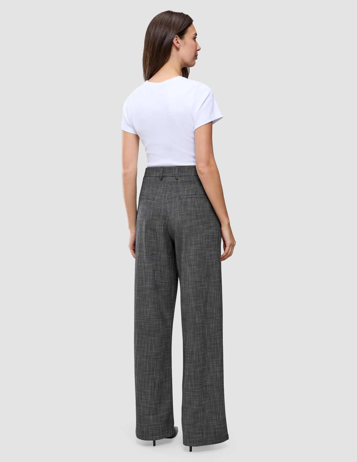 Eine Frau, von hinten gesehen, die ein weißes T-Shirt und eine graue Women Nara Pants Wide Black Check mit dezentem Gittermuster und hoher Taille trägt.