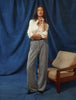 Eine Frau, die ein weißes Women’s Oxford Shirt White Orchid Slim und eine graue Hose trägt, steht vor einem blauen Stoffhintergrund.