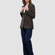 Eine Person trägt den Women Serene Blazer Regular Walnut Herringbone über einem weißen T-Shirt, dunkelblauen Jeans und braunen Stiefeletten.